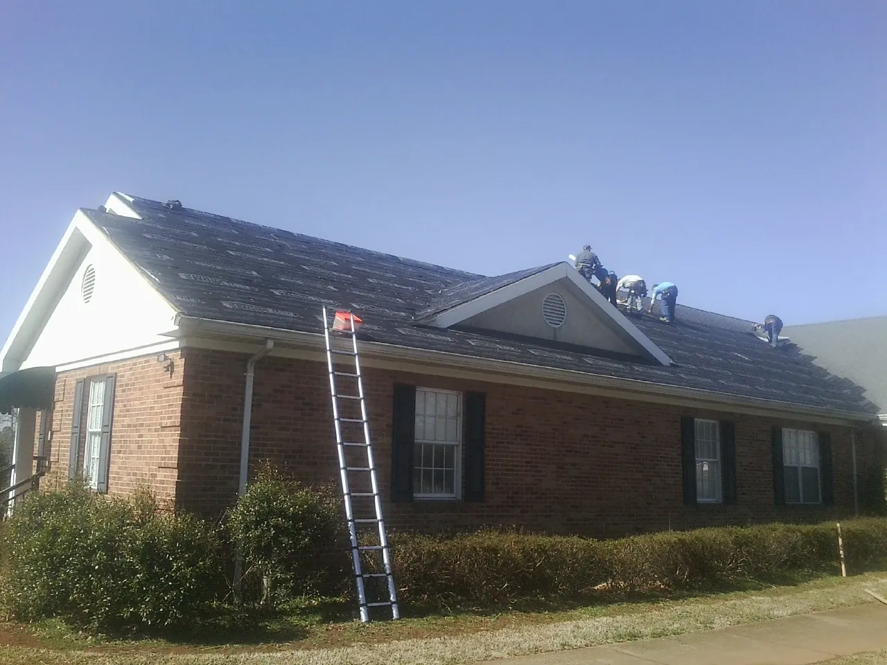 Crew tearing shingles off a brick ranch roof with a ladder set — Metal Roof Repair work by our crew in Copeland