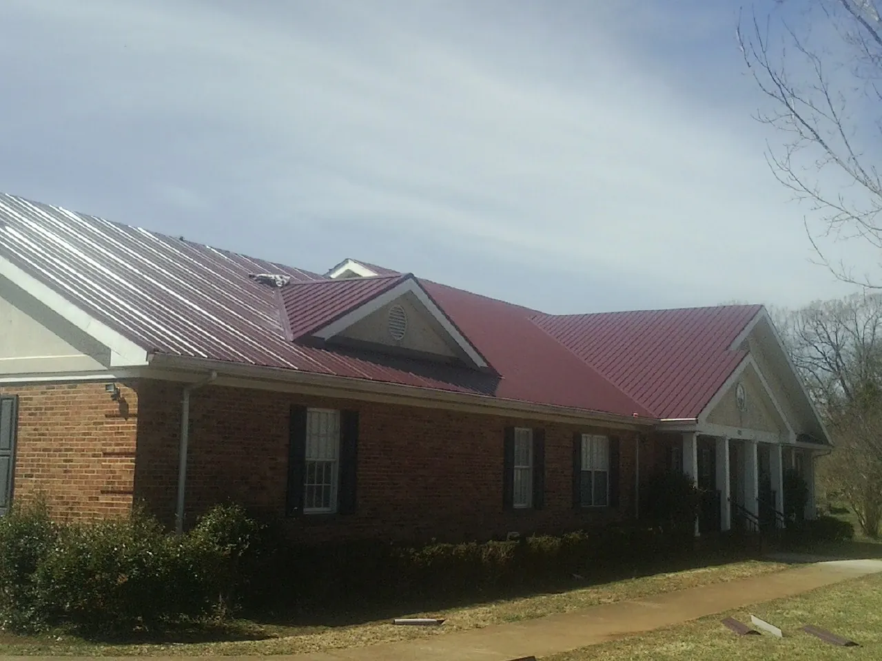 Red metal roof with gabled entries on a long brick building, from a Hail Damage Roof Repair job in Copeland