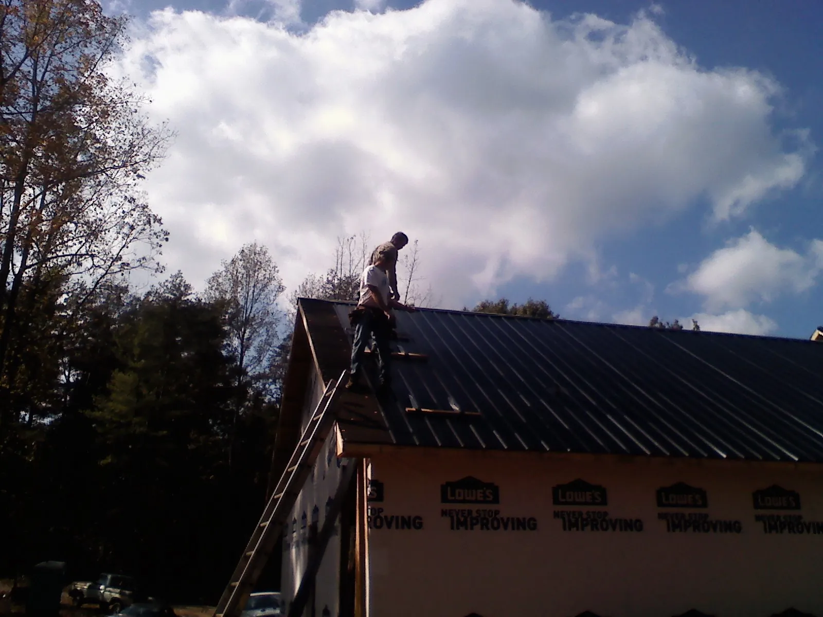 Roofer fastening dark metal panels high against a cloudy sky, from a Roof Inspection job in Copeland