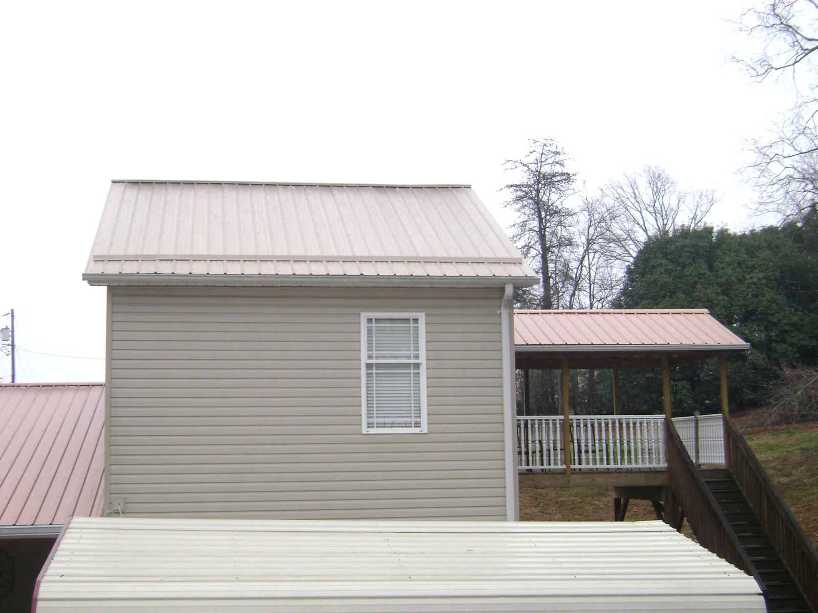 Tan metal roofs on a two story addition and attached porch, from a Roof Replacement job in Copeland